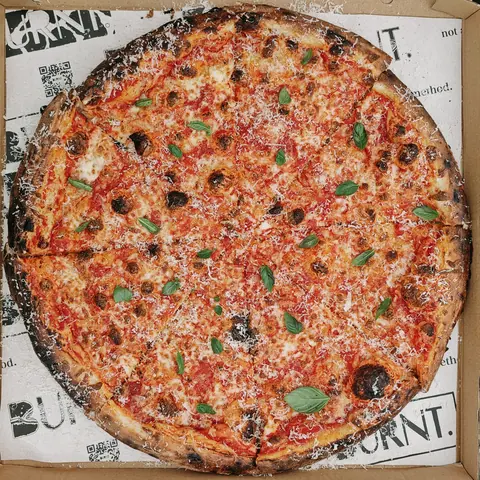 burnt. sourdough margherita pizza with basil and grated cheese in a branded box, top view